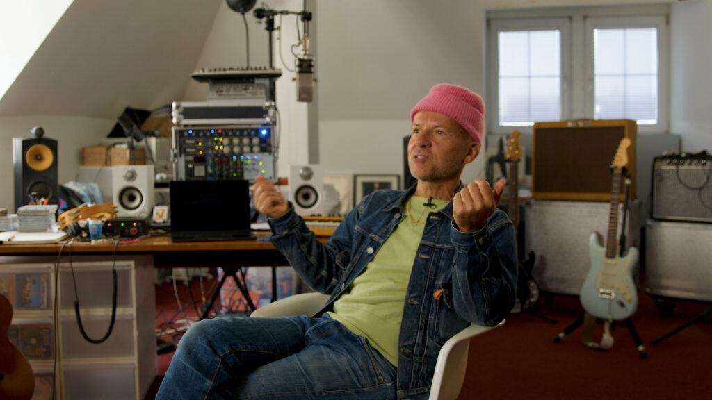 Der Musiker Shantel sitzt in seinem Studio. Im Hintergrund Instrumente und Verstärker sichtbar.