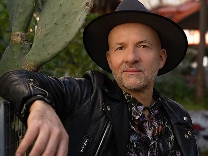 Der Musiker Shantel lehnt mit Hut in Lederjacke lässig angelehnt an eine Kaktee